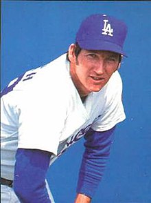 A man in a white baseball uniform with blue undersleeves and cap