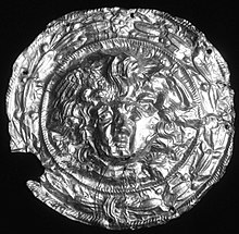 Black and white photograph of a circular gold disc with Medusa's head and hair in the centre