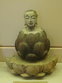 The boy Buddha rising up from lotus. Crimson and gilded wood, Trần-Hồ dynasty, 14th–15th century. Statue for worship. National Museum of Vietnamese History, Hanoi.