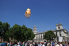 orange baby Trump balloon flown by ropes high above crowd in square