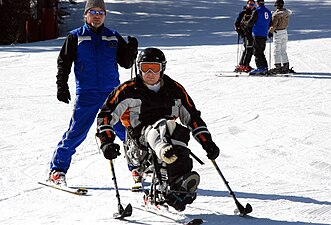 A skier with a disability on a sit-ski, using two outriggers.