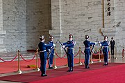 Five men in blue uniforms and silver helmets performing a rifle drill