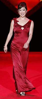a full profile of a standing woman, smiling, wearing a red dress.