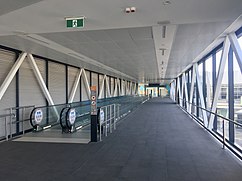 Interior of enclosed footbridge with travellators on the left. The right side has windows whereas the left side does not.