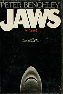 A black cover depicting a woman swimming and a shark coming towards her from below. Atop the cover is written "Peter Benchley", "Jaws" and "A Novel".