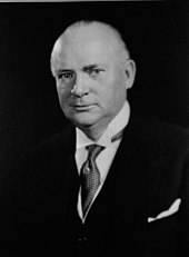 An older white man in a three piece suit, looking at the camera