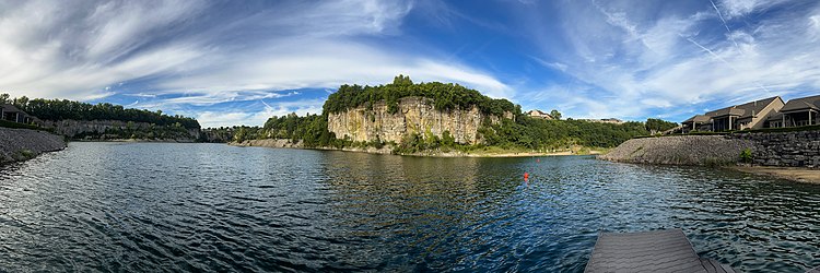 A small lake surrounded by tall limestone cliffs, with spindly trees atop the bluffs.