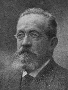 A slightly blurry black-and-white photograph of Ettore Molinari, a man with a receding hairline, narrow glasses, and full moustache and beard