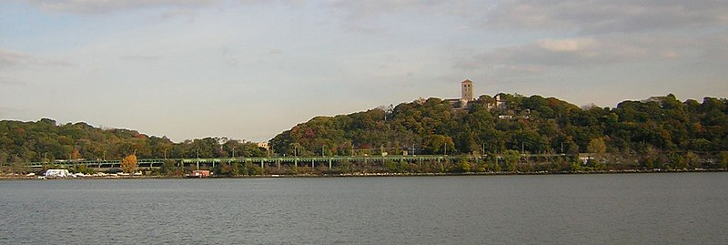 A view of the park from the Hudson River. The Cloisters museum can be seen at the top of the hill on the right. The green elevated highway is the Henry Hudson Parkway