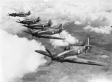 a black and white photograph of five monoplane fighter aircraft flying in formation