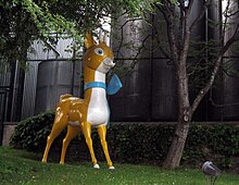 Statue with a stylistic deer in yellow and white with a blue ribbon round its neck.