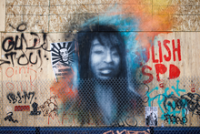 Mural of a young woman and graffiti on the other side of a chain-link fence