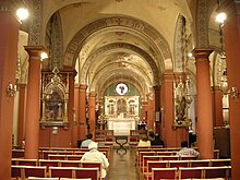 A view down the nave towards the altar. Smooth red columns support cream arches with grey-blue floral decorations. There is a round window above the altar.