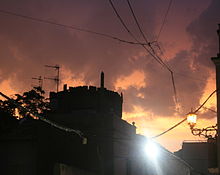 Coria sunset after rain. Sun is setting behind black silhouette of castle; and it lights heavy dark clouds from below