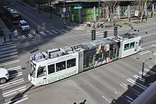 An overhead view of a white streetcar crossing an intersection, passing under traffic signals.