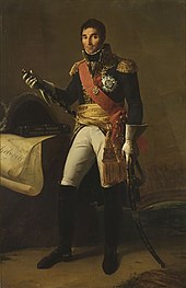 Formal full-length portrait of Masséna in dress military uniform, comprising white breeches with knee length black boots, dark cutaway coat with high collar and gold embroidery, a red shoulder sash and gold waist sash. He wears a large star of honour on his breast. He is a tall dark man with a long face and thick eyebrows. He looks quizzically at the observer and holds a marshal's baton, and sabre.