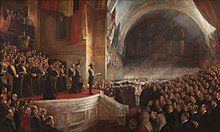 Painting of a group of people stand on a stage, a sea of people looking on. The Duke of Cornwall and York in a naval uniform stands at the front of the stage. Behind him are two women in mourning black for the death of Queen Victoria.