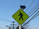 A pedestrian crossing sign in the United States with solar-powered lit outline.