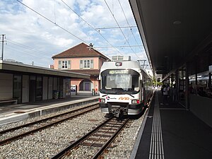 White train on double track with two-story station building in the background