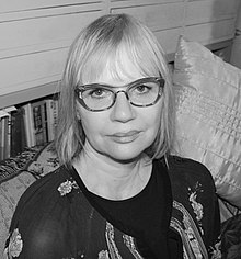 Gaele Sobott sitting in a room with cushions and bookshelf in the background