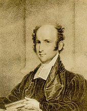 A man, bald on top with thick tufts of hair on either side of his head, wearing a black robe and white shirt