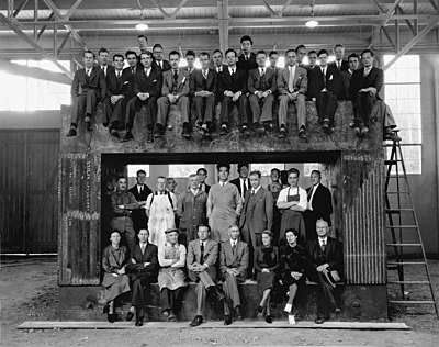 A group of men pose in front, around, and on a large metal structure.