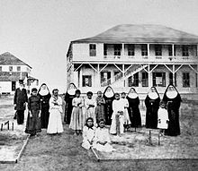 Photograph of a number of Sisters of St. Francis standing with some girls and Walter Murray Gibson in front of the Kapiolani Home for Girls