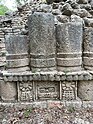 Three stone pillars, aged and a few feet tall sit atop intricate stone carved foundation depicting a face in the center and two flowers on either side