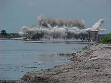 A color photograph of a large cement structure on the C-38 Canal being destroyed with explosives