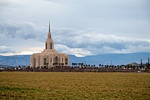 A landscape picture of the Red Cliffs temple, with a large field leading to the temple. Mountains can be seen in the distance along with rolling clouds.