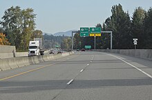 A four-lane freeway with concrete barriers seen with little traffic and a sign gantry ahead.