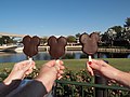 Three outstretched hands old popsicle sticks holding ice cream bars shaped like the silhouette of Mickey Mouse's head