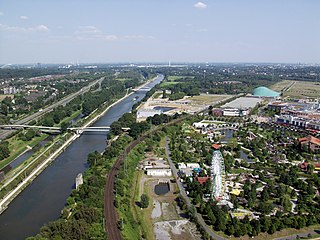 Blick vom Gasometer in Oberhausen. Rechts auf dem Bild sieht man Teile des Einkaufszentrums CentrO mit Park. Links davon verläuft der breite Rhein-Herne-Kanal, weiter links vom Kanal ist die Emscher und noch weiter links die Autobahn 42 (Emscherschnellweg).