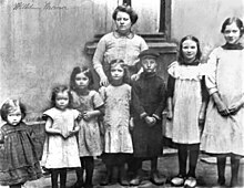 Witwe Wilhelmine Krämer mit ihren wie Orgelpfeifen aufgestellten 7 Kindern vor der Werkswohnung Phönix AG, für die sie kostenloses Wohnrecht erkämpfte. Schwarz-Weiß-Foto