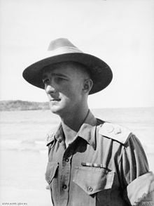 a half-profile of a male wearing a broad-brimmed hat with the brim turned down, with a beach in the background