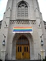 Pride flag banner hung over the entrance to the Church of the Pilgrims in Washington, D.C. with the words "ALL ARE WELCOME" printed underneath