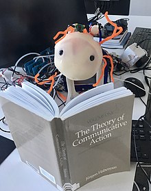 Image of Hitodama, soft telerobot reading a book by Jürgen Habermas.