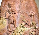 Victory Stele of Naram-Sin, c. 2230 BC. It shows him defeating the Lullibi, a tribe in the Zagros Mountains, and their king Satuni, trampling them and spearing them. Satuni, standing right, is imploring Naram-Sin to save him.[61] Naram-Sin is also twice the size of his soldiers.
