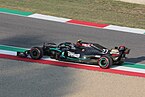 A black Formula One car drives between some gravel and some tarmac on a paved area painted in the colours of the Italian flag.