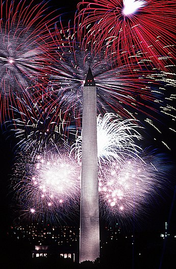 Photograph of red, white, and blue fireworks lighting the night sky behind the Washington monument in 1986