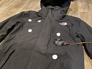 Bullet hit locations marked out with white stickers. An assembled device is placed temporarily on the costume for reference.