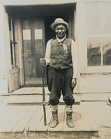 Tonené with a rifle, standing on a porch
