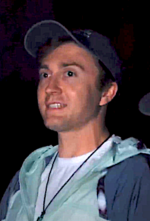 Daryl Sabara in a cap, t-shirt, and jacket, looking towards his right side