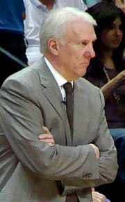 Greg Popovich with his arms crossed and a stern expression