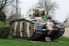 A tank painted with green and brown camouflage colours sits on a hard stand. There is an inscription plaque in front of it.