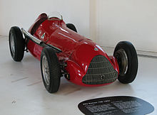 a red vintage open-wheel racing car in a museum