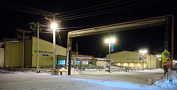 A utilidor system is used in Utqiaġvik, Alaska due to extensive permafrost underlying the city. At right foreground is a portion of the utilidor crossing Okpik Street overhead, adjacent to Barrow High School.