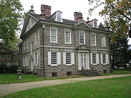 Photo shows the front and left side of a two-story stone house.
