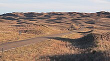 Dune-like hills covered with brown grass; highway running through foreground