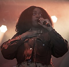 Noname onstage smiling, holding a microphone